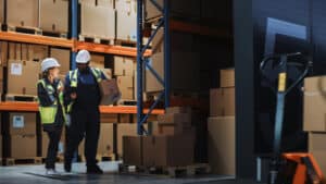 two warehouse workers looking at a tablet in the aisle of warehouse