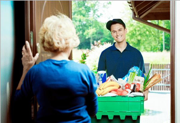 smiling delivery boy handing groceries to elderly customer