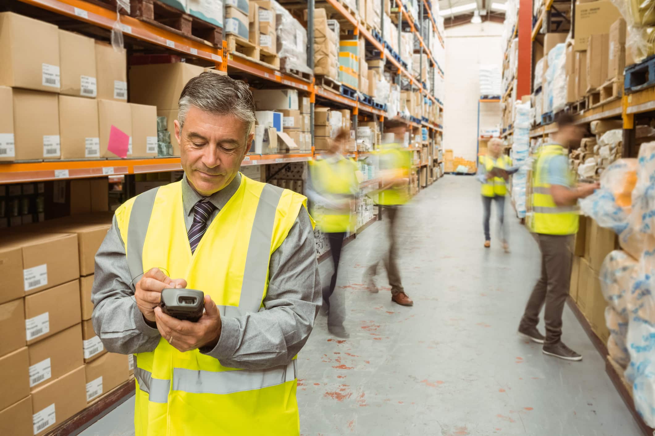 male warehouse manager checking stock with team behind him working