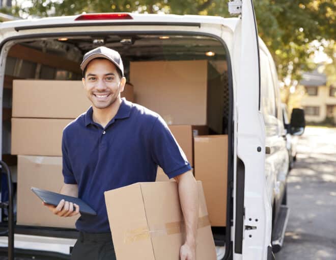 smiling delivery driver holding boxes in front of full truck