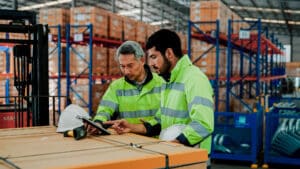 hybrid workers in a warehouse discussing something on an ipad