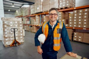 Guy with glasses in warehouse with forklift behind him