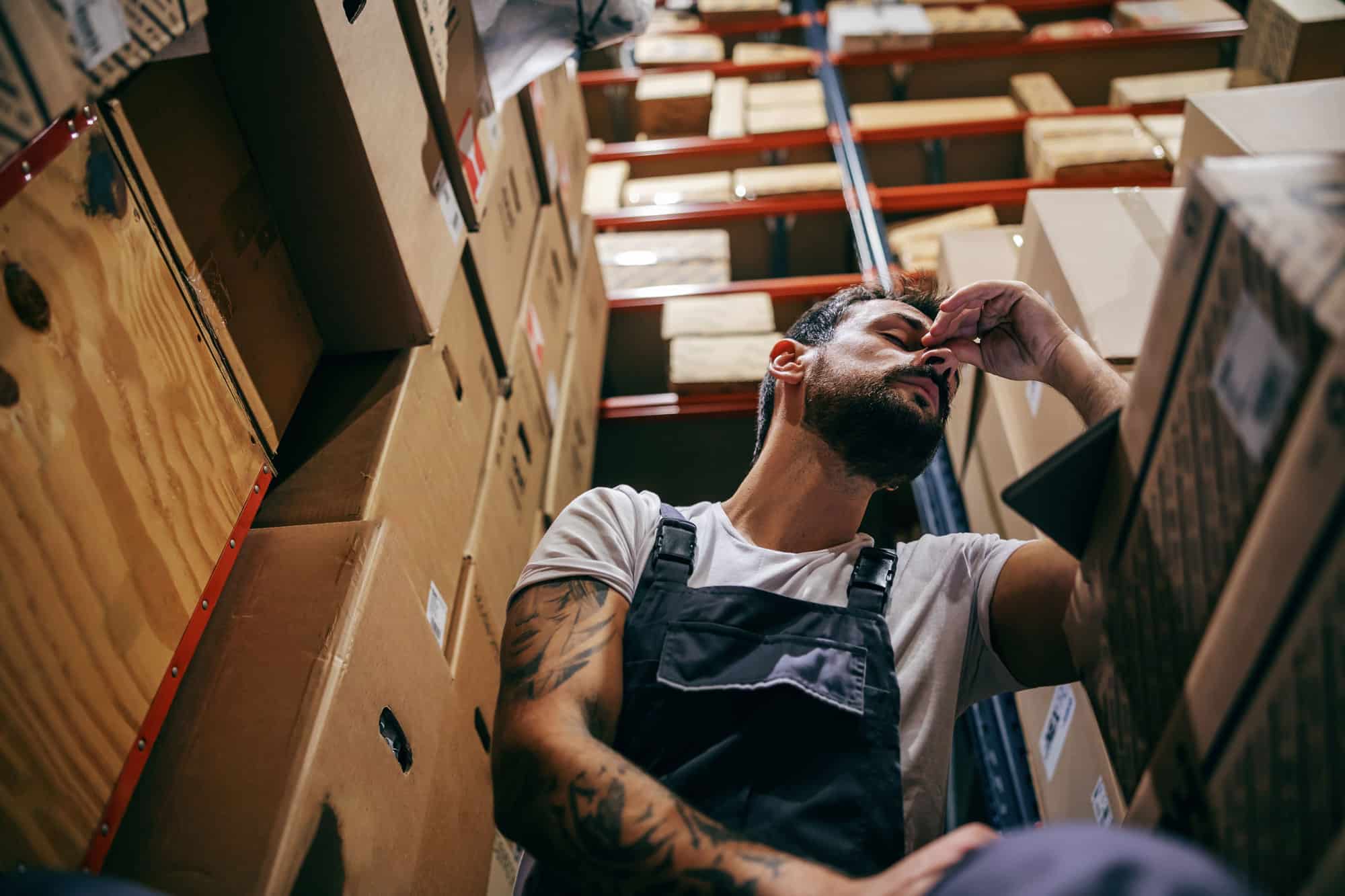 Tired Man Sitting in Warehouse Surrounded by Boxes