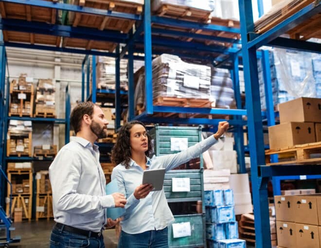 managers in warehouse discussing inventory using technology