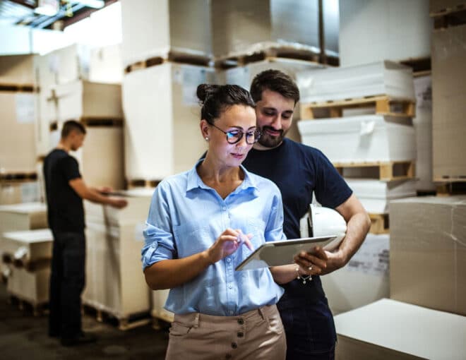 Warehouse employees analyzing real-time data on a tablet to improve supply chain visibility.