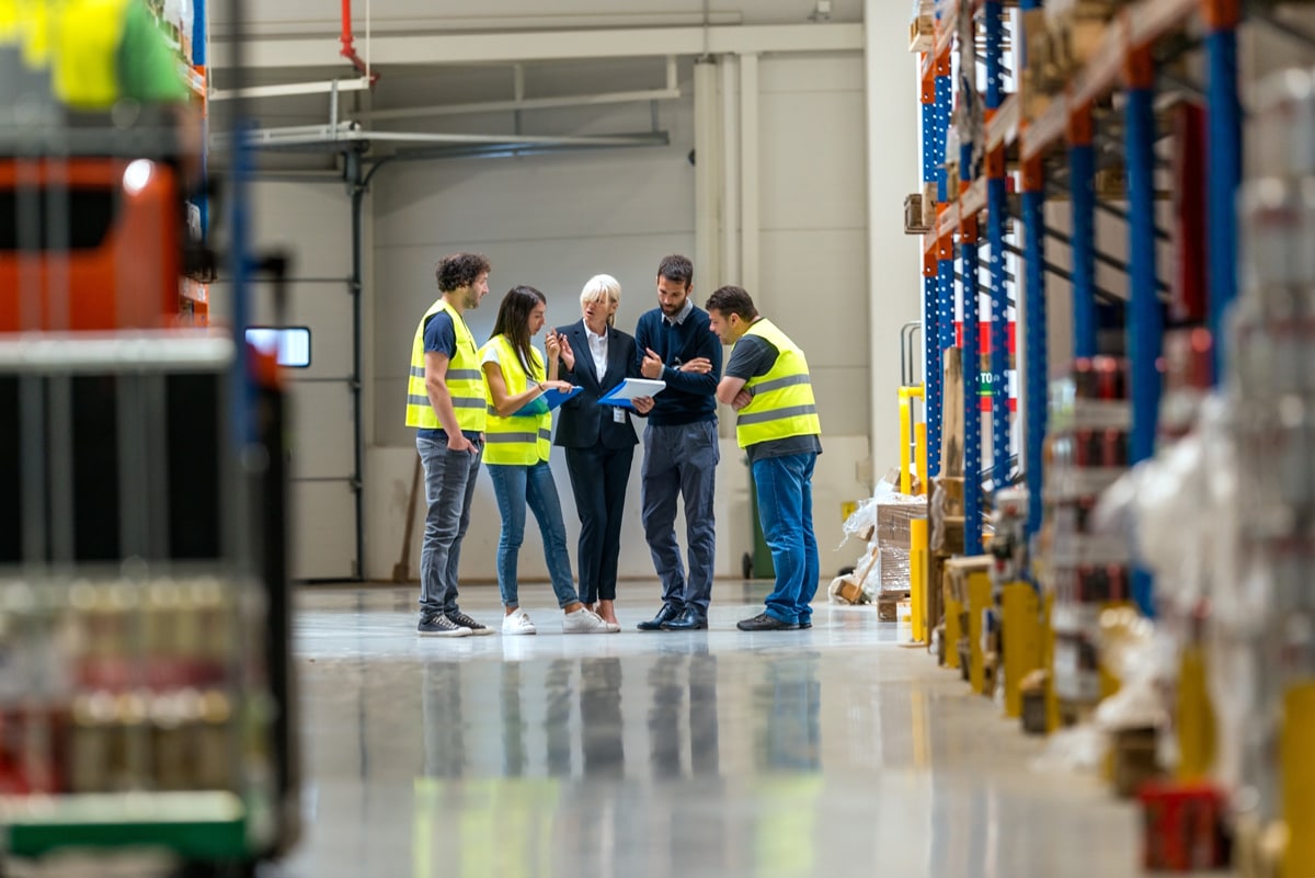 warehouse workers gathered around a corporate worker looking at information