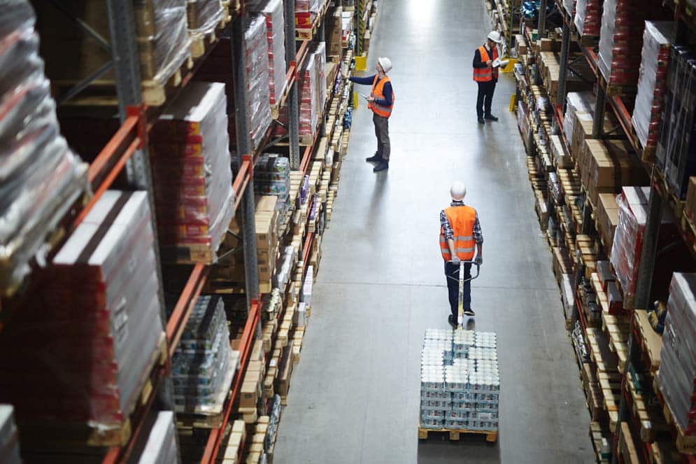a view in to a busy warehouse with an associate pulling a manual forklift