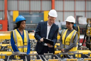 Warehouse supervisor collaborating with associates beside a manufacturing conveyor belt