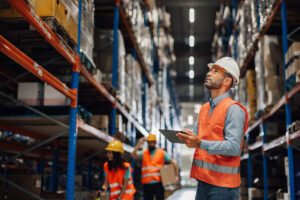 Warehouse manager reviewing information on a tablet while warehouse pickers in the background