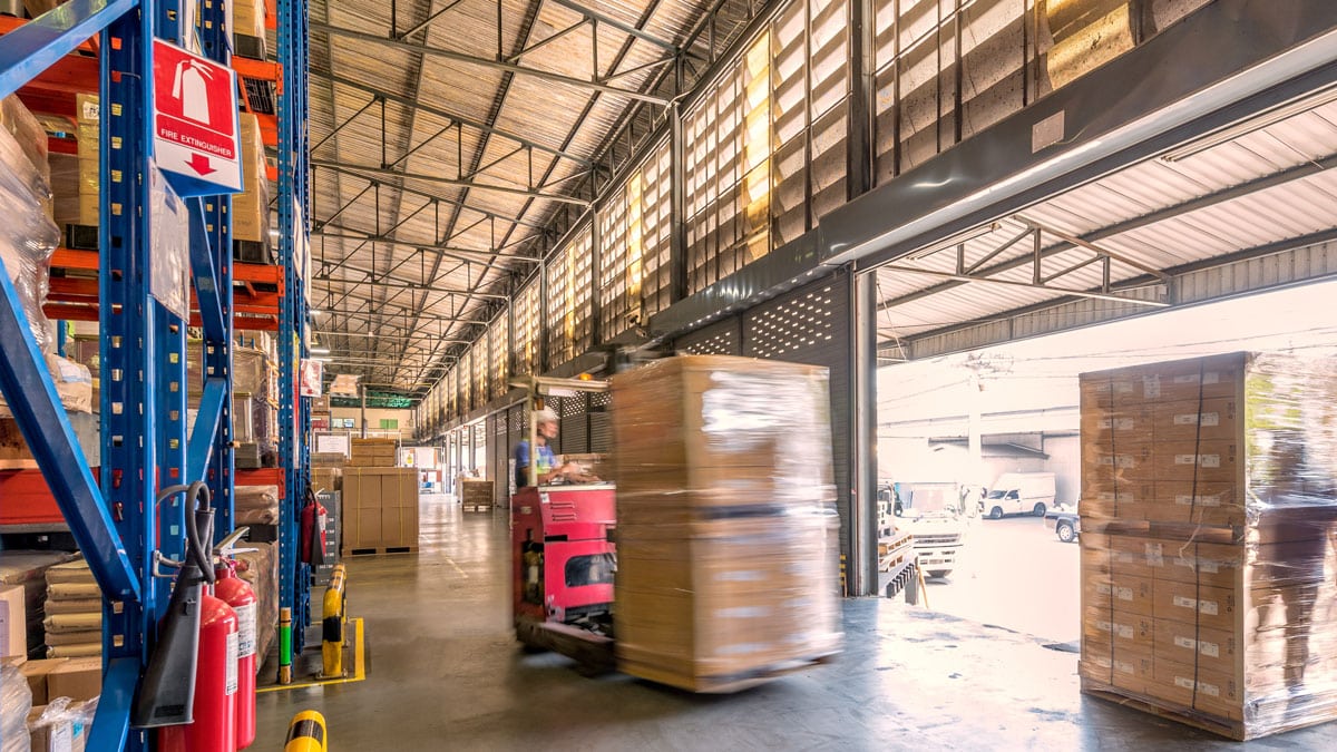 Warehouse worker moving a shrink-wrapped pallet with a forklift near an open loading dock
